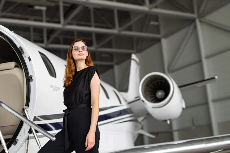 Confident woman in black attire and sunglasses standing beside a Cessna Citation XLS jet inside a hangar, representing the luxury and lifestyle of an owner club experience.