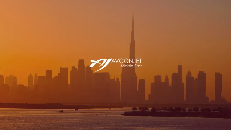 Dubai skyline at sunset with the Burj Khalifa rising above dark silhouetted towers and calm water in the foreground. White logo text reading "AVCON JET Middle East" overlays the center of the skyline.